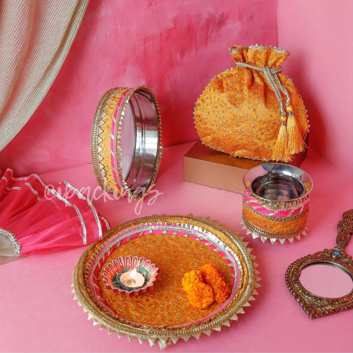 Decorative items including a potli bag, bangles, and a tray on a pink background