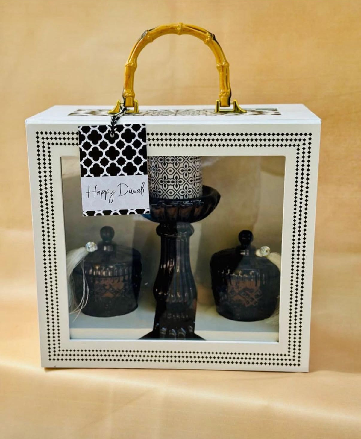 Decorative set with black candle holders and a white box with gold handle on a beige background